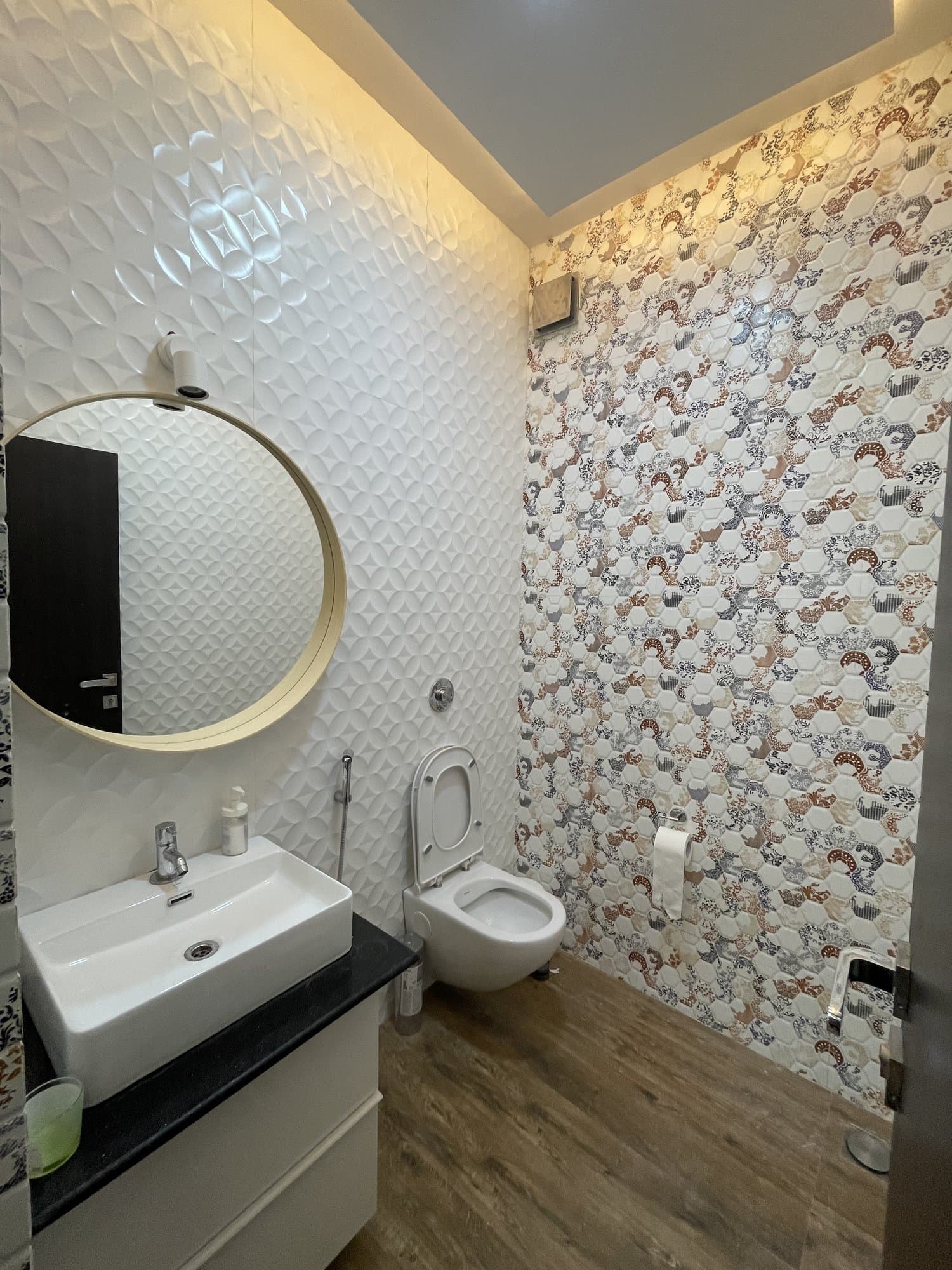 The transformed bathroom — a patterned tile feature wall, round mirror and wall-hung fixtures
